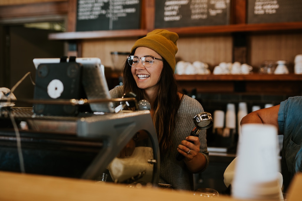 Girl behind bar, holding portafilter and smiling